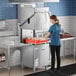 A commercial high temperature door type dishwasher with a ventless design being operated by a person in a kitchen setting.