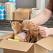 A person opening a cardboard box with a HexaFil Expanding Void Fill Paper Dispenser inside.