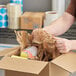 A person using a HexaFil Mini expanding void fill paper dispenser to open a cardboard box with paint inside.