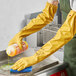A person wearing Showa yellow rubber gloves cleaning a countertop with a bottle of cleaning liquid.