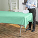 A person holding a white plate on a table with a mint green plastic table cover.