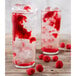 A pair of glasses with ice and red liquid and raspberries.