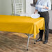 A person holding a yellow plastic table cover over a table.