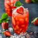 A glass of strawberry lemonade with ice garnished with a strawberry.