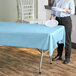 A person holding a white plate over a light blue plastic table cover on a table.