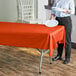 A woman standing next to a table with a tangerine plastic table cover on it holding a white plate.