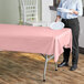 A person holding a white plate over a pink plastic covered table.