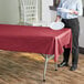 A person holding a white plate over a Choice burgundy plastic table cover on a table.