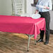 A woman holding a white plate over a hot pink table covered with a plastic tablecloth.