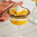 A glass bowl of dessert with mango filling topped with whipped cream.