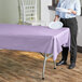 A woman holding a white plate over a lavender plastic table cover on a table.