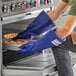 A person wearing blue gloves and using Tucker Safety QuicKlean gloves to put a tray of food in an oven.