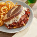 A plate with a sandwich made with Unreal Deli plant-based corned beef slices, cheese, and onion rings.