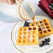 A Tablecraft almond dispenser top on a container pouring syrup over a waffle.