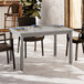 A Grosfillex Sigma volcanic black aluminum dining table with chairs underneath.