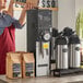 A man in an apron pouring coffee beans into a Grindmaster Slimline coffee grinder on a counter in a coffee shop.