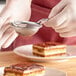 A person using a Matfer Bourgeat stainless steel fine mesh strainer to sprinkle powdered sugar over a piece of cake.