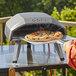 A person using an Ooni Koda 12 outdoor pizza oven to cook a pizza on a table on a patio.