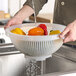 A person washing yellow peppers in a Giganplast colander.