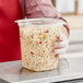 A person holding a Pactiv plastic deli container of pasta salad.