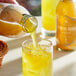 A person pouring Harney & Sons American Buzz Organic Turmeric Orange Iced Tea into a glass with ice.