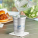 A silver Ball aluminum cup with ice cubes on a table being filled with water.