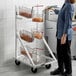 A woman standing next to an Assure Parts mobile fryer basket rack filled with fryer baskets.