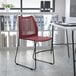 A Flash Furniture burgundy stacking chair with a black sled base in a room with a white table and shelves.