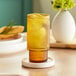 An Acopa Lore amber highball glass with a lemon slice on the rim, on a coaster.