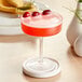 A Coupe glass with a red cocktail and fruit garnish on a white plate.