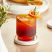 An Acopa amber rocks glass filled with a drink and garnished with an orange slice.