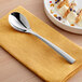 An Acopa stainless steel dessert spoon on a napkin next to a bowl of food.