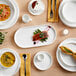 A table with white plates and Acopa Lore stainless steel dessert spoons.