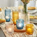 A group of Acopa blue glass tealight holders with lit candles on a table with flowers.