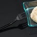A close-up of a Fineline black plastic tasting fork with food on it.