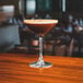 An Arcoroc Romeo coupe glass filled with brown liquid on a table.