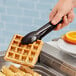 A person using Carlisle black plastic utility tongs to hold a waffle.