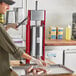 A woman using a Tre Spade manual sausage stuffer on a butcher shop counter.