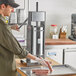 A man using a Tre Spade stainless steel sausage stuffer on a countertop to make sausages.