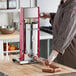 A person wearing gloves uses a Tre Spade manual vertical sausage stuffer to prepare sausages.