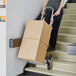 A man using a Lavex aluminum stair climber hand truck to move a box up some stairs.