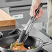 A person cooking food in a pan with Choice 12" Silicone Tip Locking Tongs with a black handle.