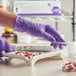 A person wearing Kimtech purple gloves puts a tube of pills into a container.