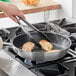 A hand using tongs to cook meat in a Choice aluminum non-stick fry pan.