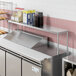 An Avantco stainless steel single deck overshelf on a counter with a group of containers with white labels.