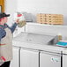 A man wearing an apron using an Avantco stainless steel overshelf over a counter.