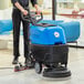 A person standing behind a blue and black Lavex walk behind floor scrubber machine with scrub brush in a corporate office cafeteria.