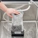 A person using a Hamilton Beach commercial container rinser to wash a glass container over a sink.