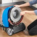 A woman using a Lavex corded walk behind floor scrubber to clean a floor.