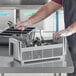 A man in a black apron using a Cambro 8 Compartment Camrack flatware basket to hold utensils.